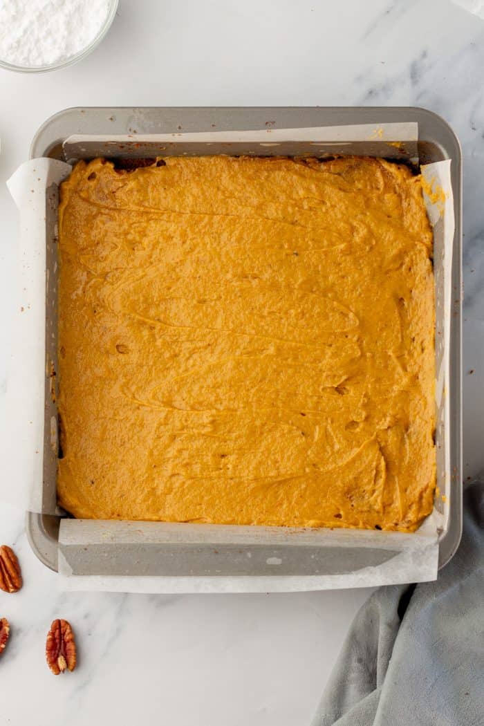 The pumpkin cake batter in a cake pan with parchment paper.