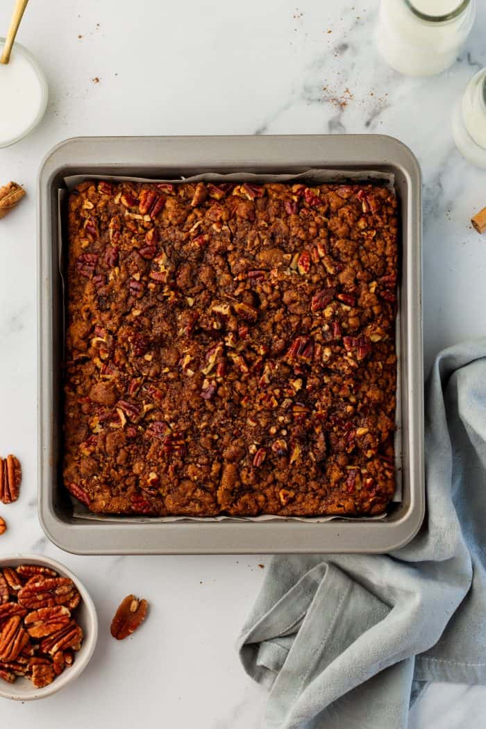 Baked pumpkin pecan coffee cake in a cake pan with a grey napkin beside it.