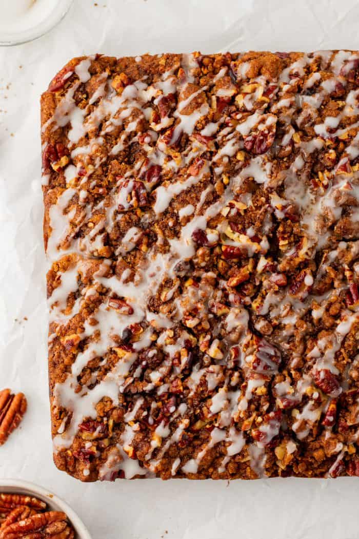 Baked pumpkin pecan coffee cake that has been removed from the cake pan with icing drizzled all over it.