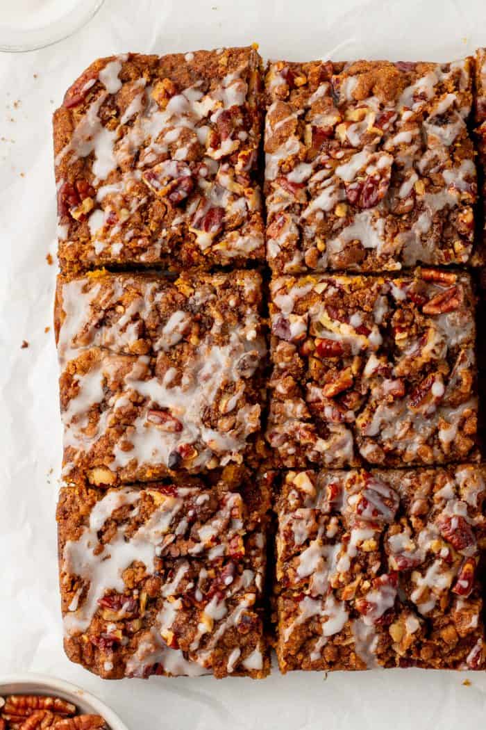 Baked pumpkin pecan coffee cake that has been removed from the cake pan with icing drizzled all over it and sliced into squares.