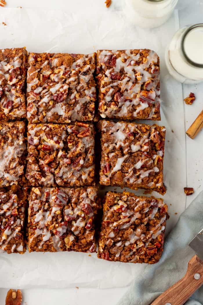 Baked pumpkin pecan coffee cake that has been removed from the cake pan with icing drizzled all over it and sliced into squares.