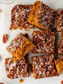 Baked pumpkin pecan coffee cake that has been removed from the cake pan with icing drizzled all over it and sliced into squares.