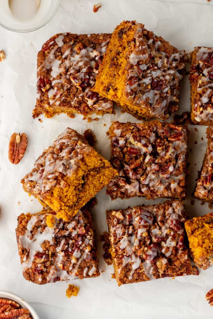 Baked pumpkin pecan coffee cake that has been removed from the cake pan with icing drizzled all over it and sliced into squares.