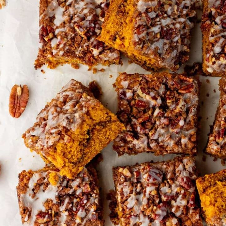 Baked pumpkin pecan coffee cake that has been removed from the cake pan with icing drizzled all over it and sliced into squares.