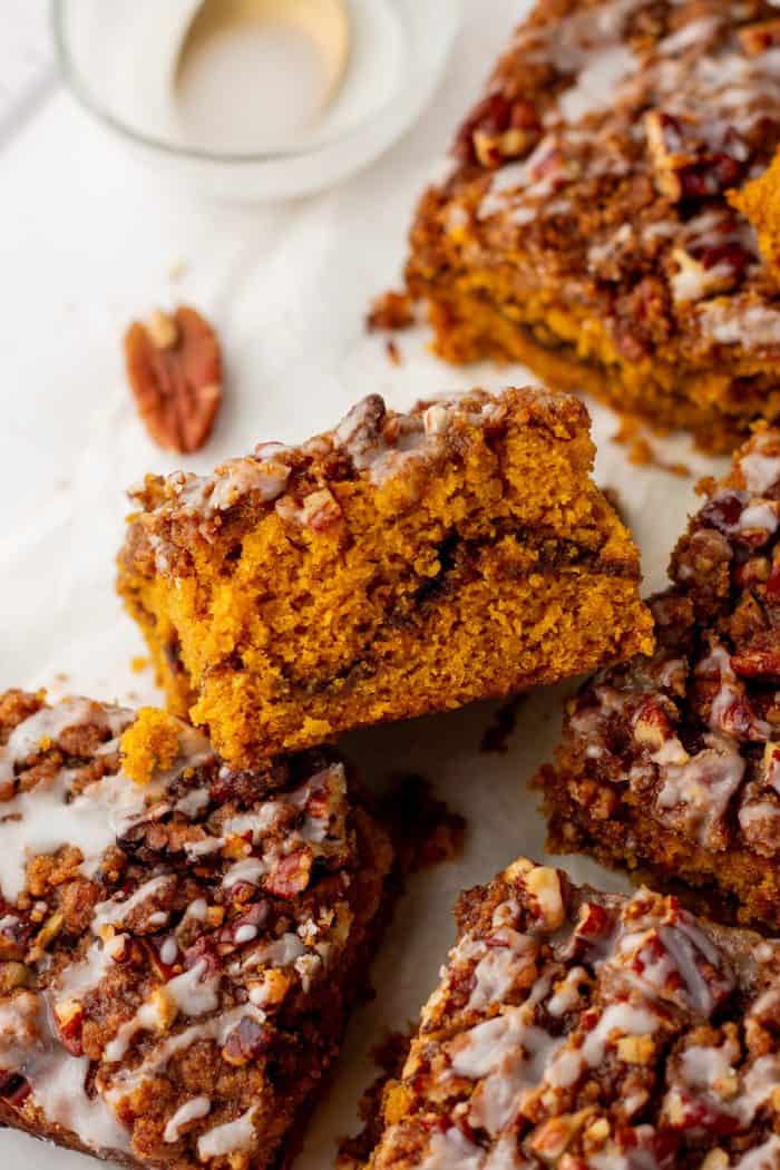 Baked pumpkin pecan coffee cake that has been removed from the cake pan with icing drizzled all over it and sliced into squares.