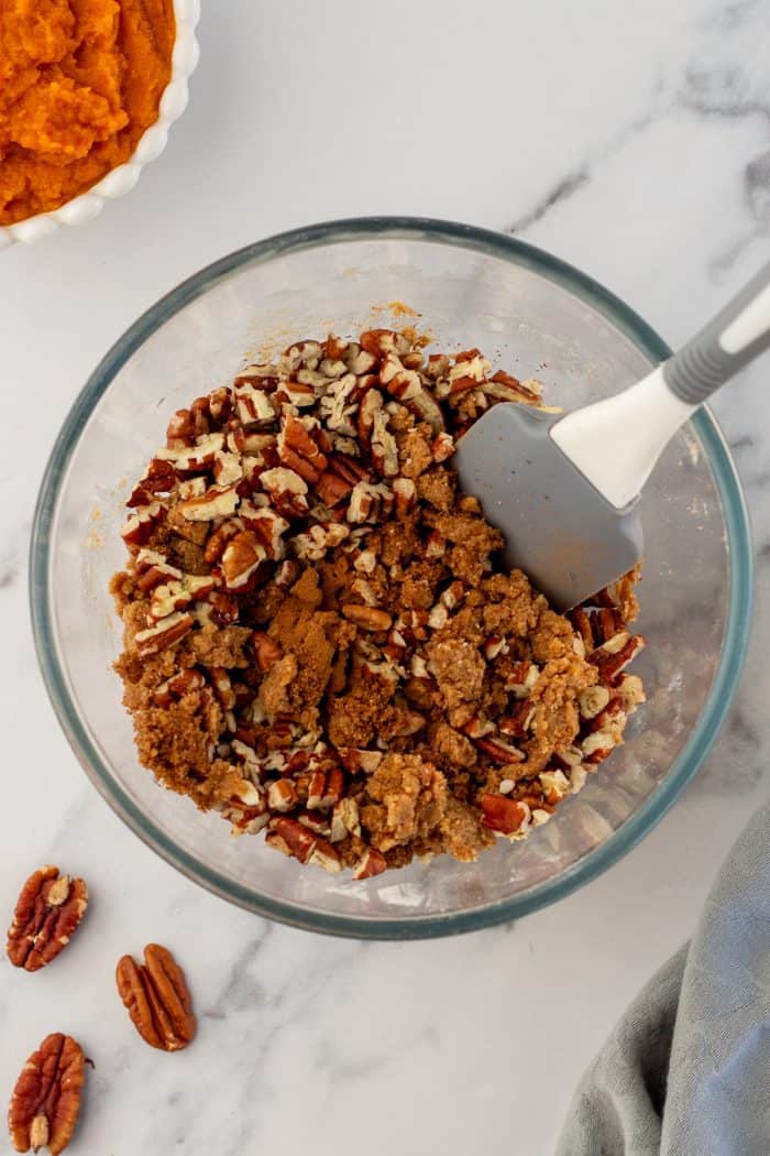 Brown sugar, cinnamon, butter, flour, and pecans mixed together in a glass bowl.