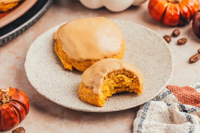 Two pumpkin spice latte cookies on a plate and one has a bite taken out of it.