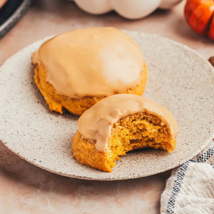 Two pumpkin spice latte cookies on a plate and one has a bite taken out of it.