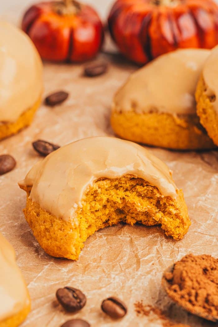 A few pumpkin spice cookies with latte icing on a brown surface and one has a bite taken out of it.