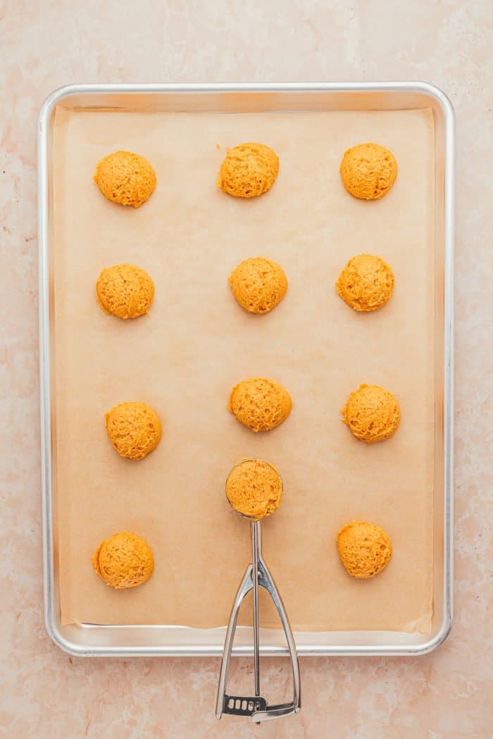 A baking sheet with parchment paper and scoops of unbaked pumpkin pie cookies.