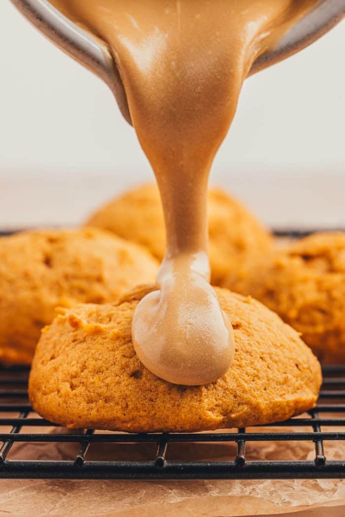 Latte icing being poured on pumpkin spice cookies.