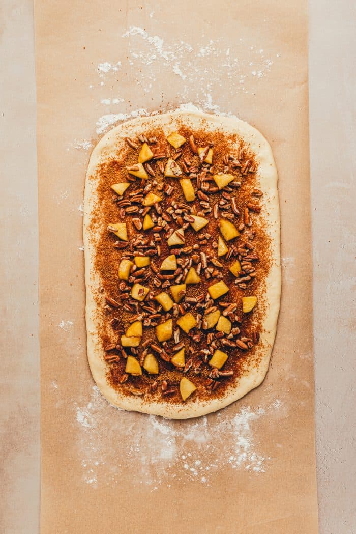 Cinnamon roll dough rolled out with cinnamon brown sugar, and chopped apples sprinkled over it.