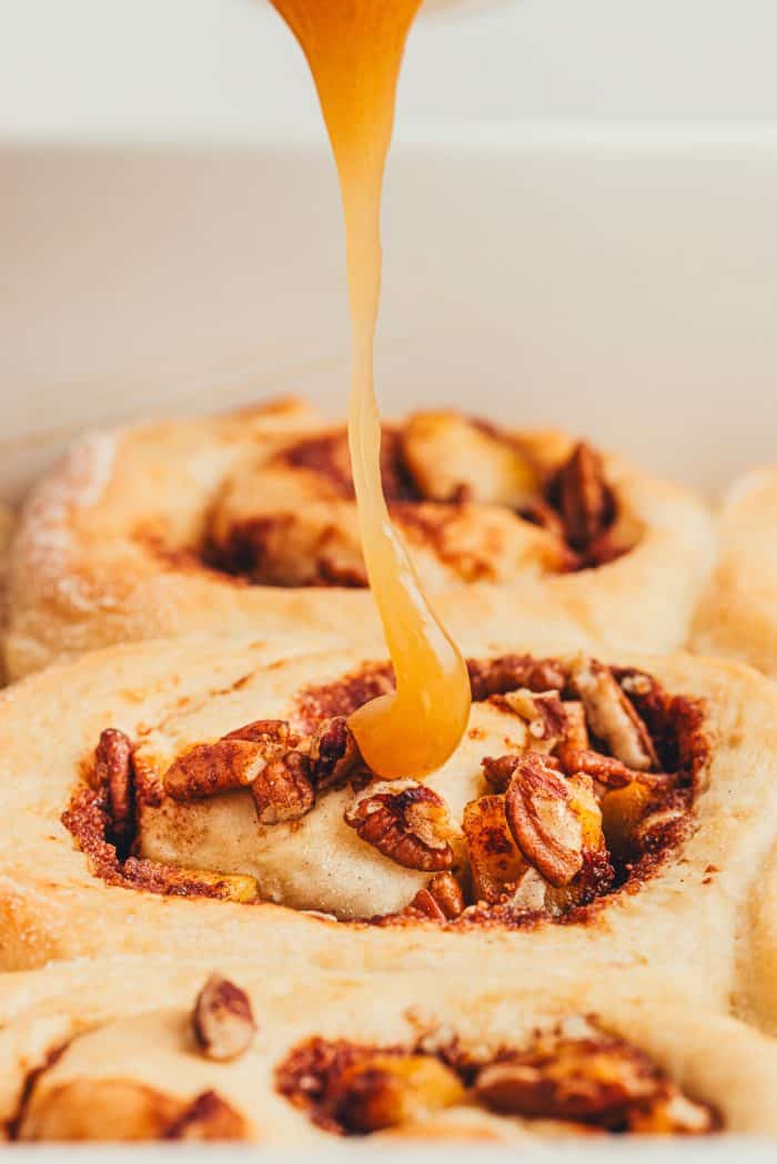 Apple cinnamon rolls with caramel sauce being drizzled over them.