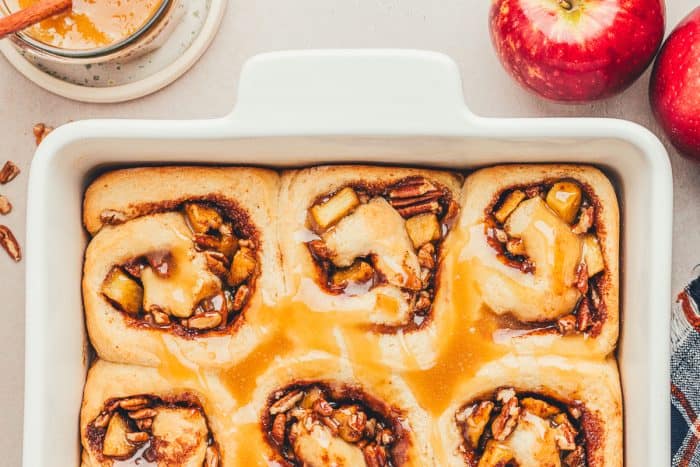 A white baking pan with baked cinnamon rolls with caramel sauce drizzled over them.