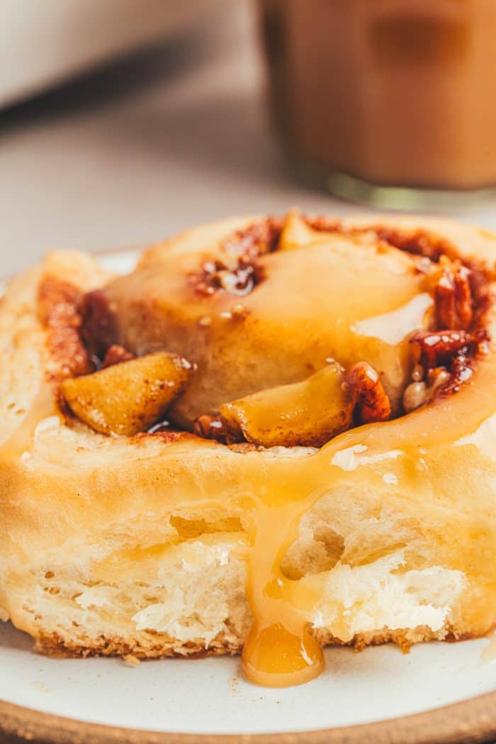 A closeup of a caramel apple cinnamon rolls on a white plate.