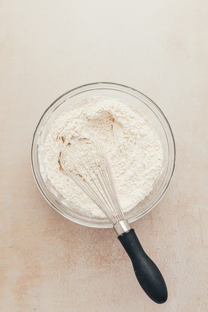 A glass bowl with flour and a whisk.