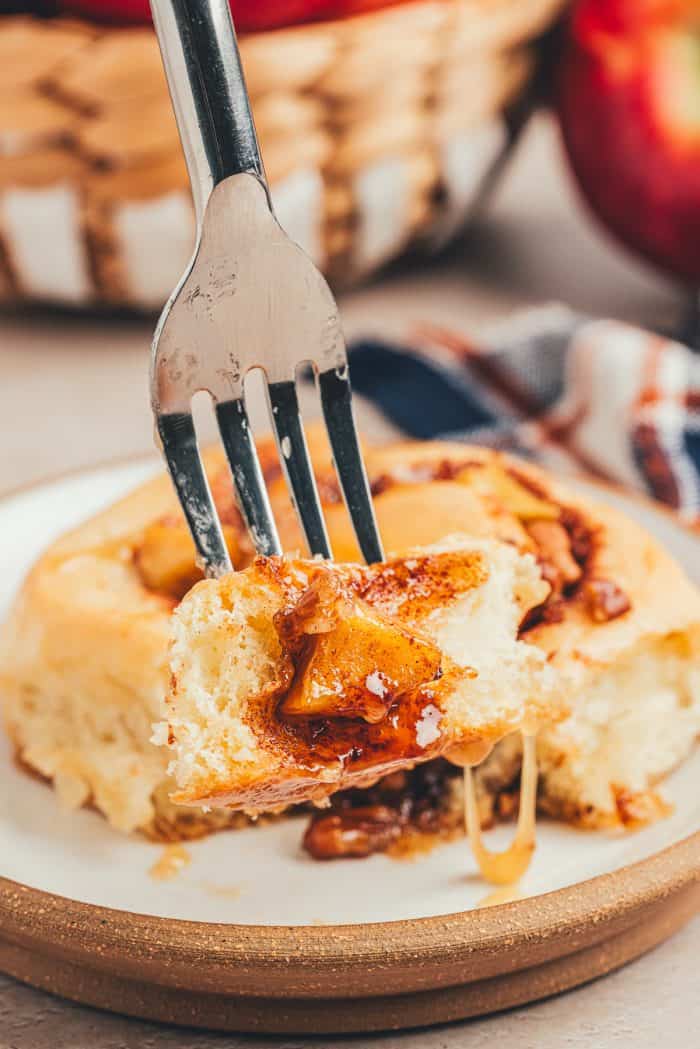 A closeup of a caramel apple cinnamon rolls on a white plate with a fork going through it.