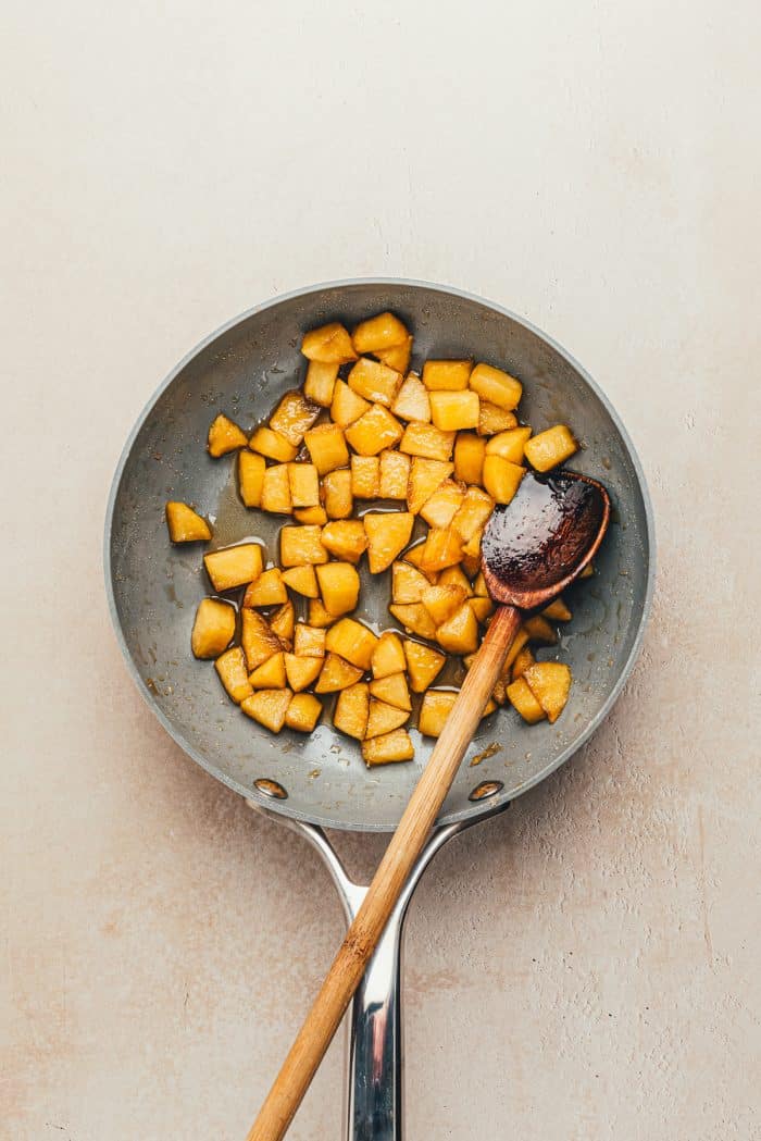 A skillet with cooked apples and a wooden spoon.