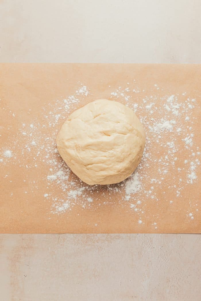 The cinnamon roll dough on a wooden board with flour sprinkled around it.