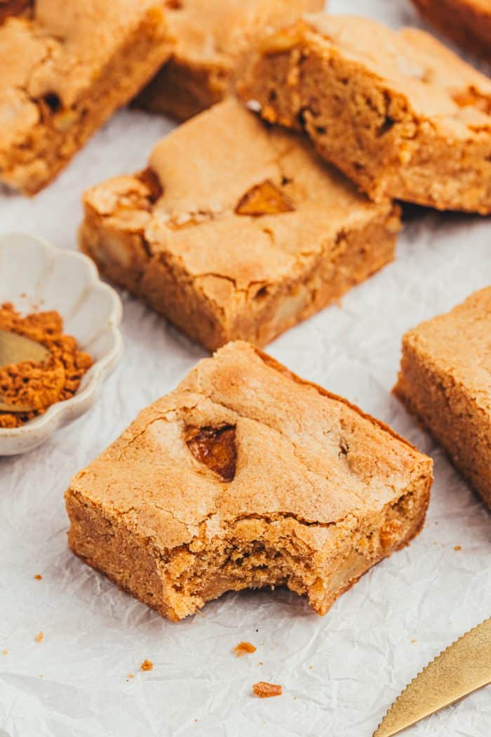 A few apple pie blondies scattered on a counter with one Blondie with a bite out of it.