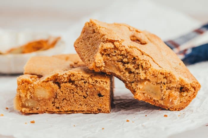 Two apple pie blondies beside themselves and one has a bite taken out of it.