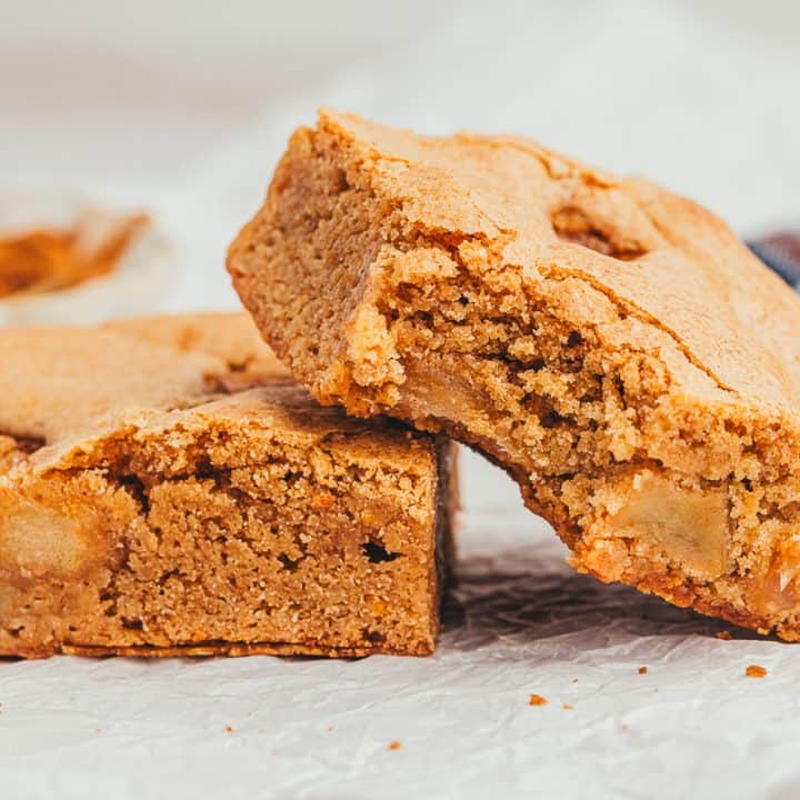 Two apple pie blondies beside themselves and one has a bite taken out of it.