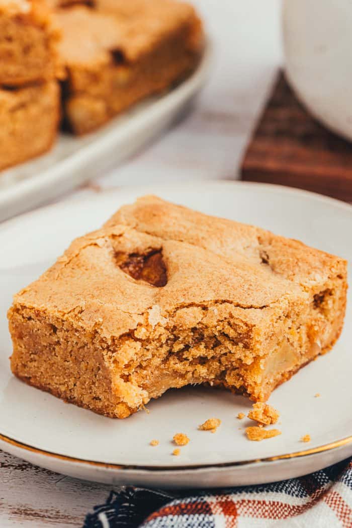 A slice of Apple Blondie with a bite taken out of it on a white plate.