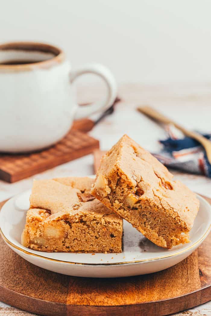 A white plate with two Apple Blondies and a cup of coffee in the background.