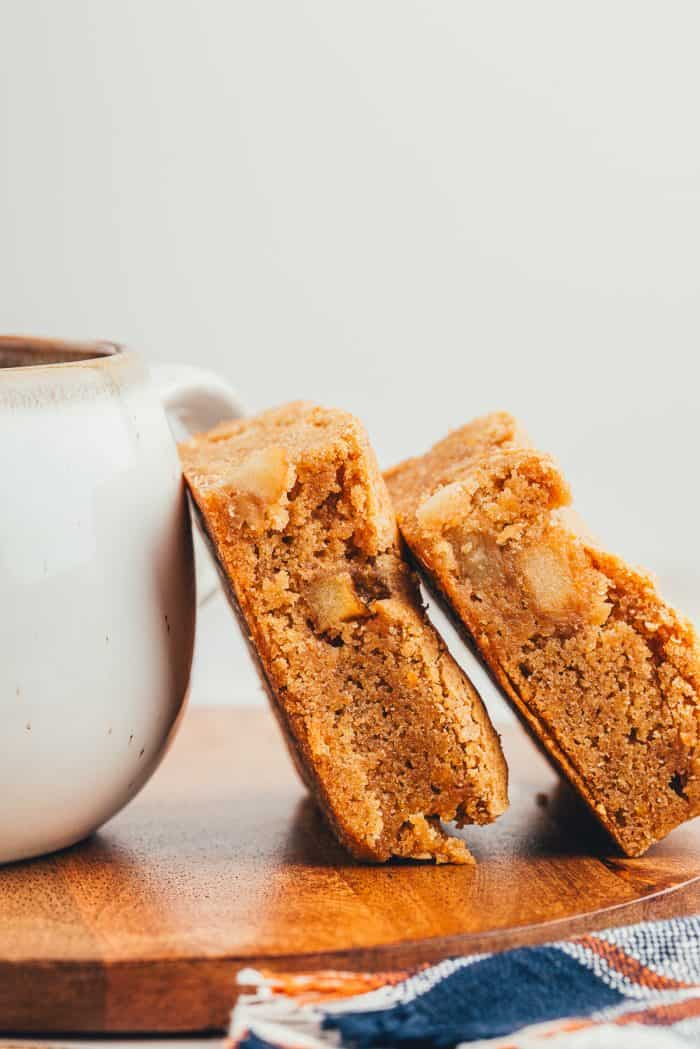 Two apple pie blondies leaning against a cup of coffee.