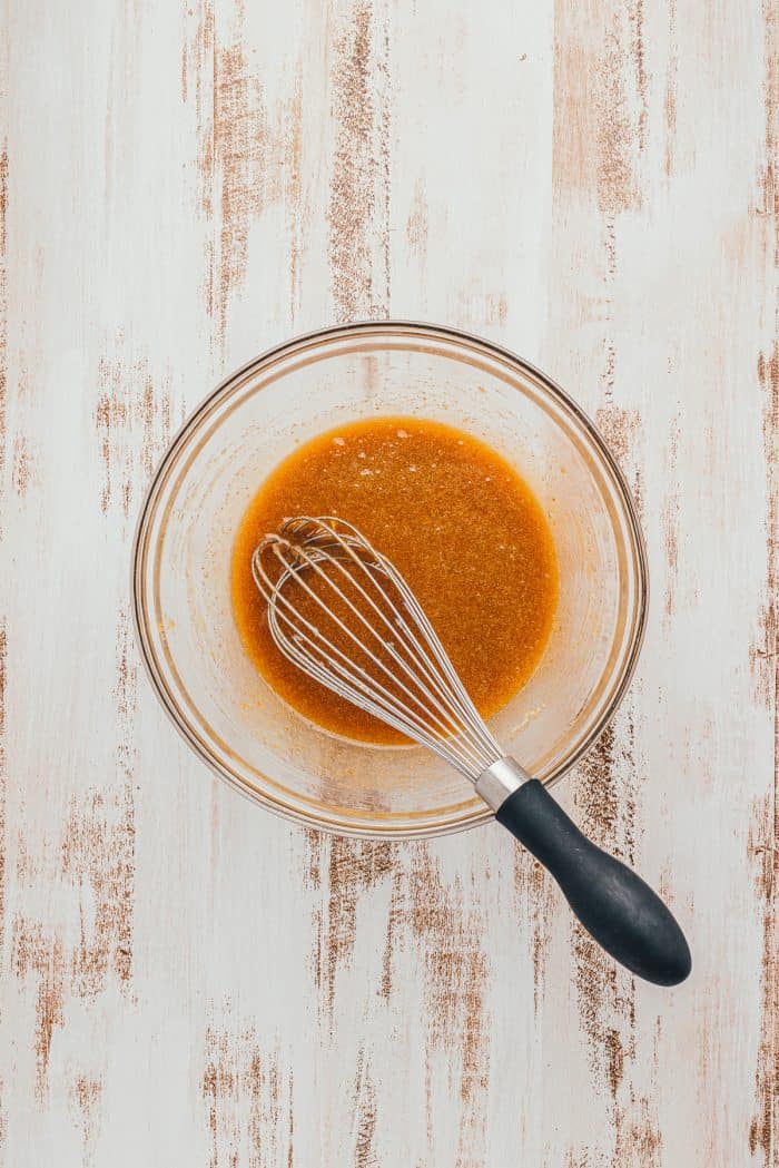 A glass bowl with the wet ingredients for Apple Blondies and a whisk.