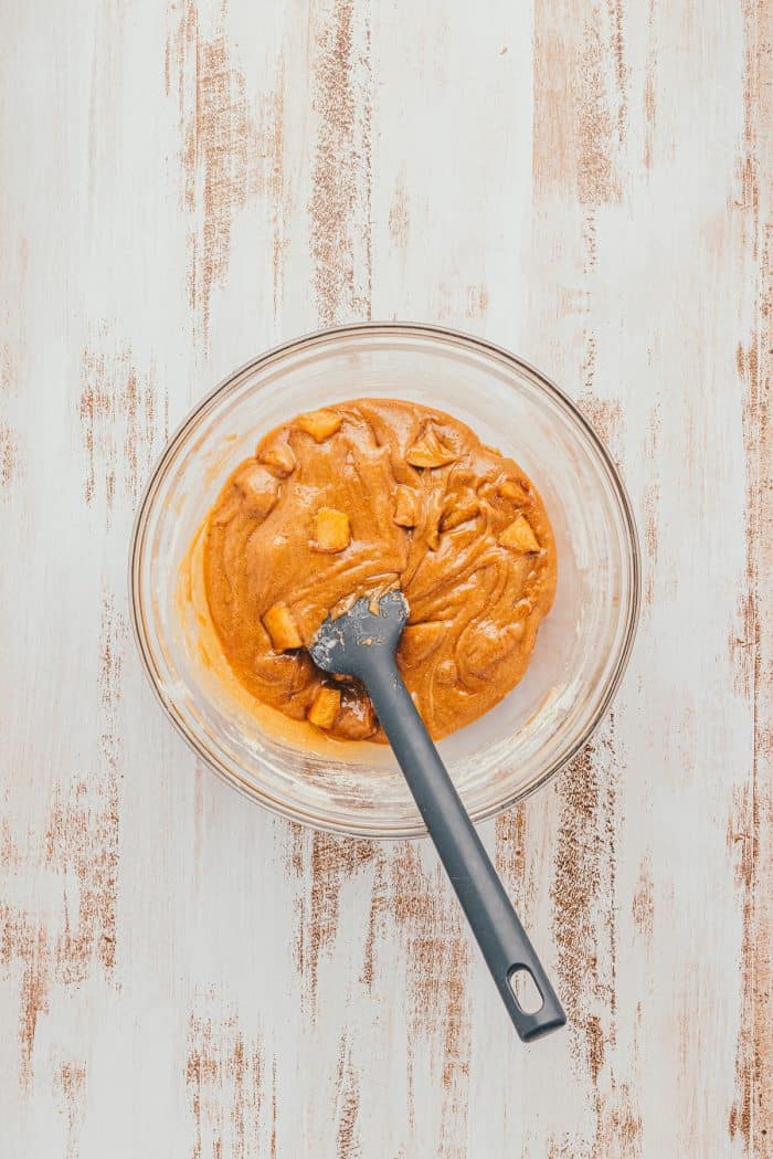 The batter for Apple Blondies with cubed apple in a glass bowl with a spatula.