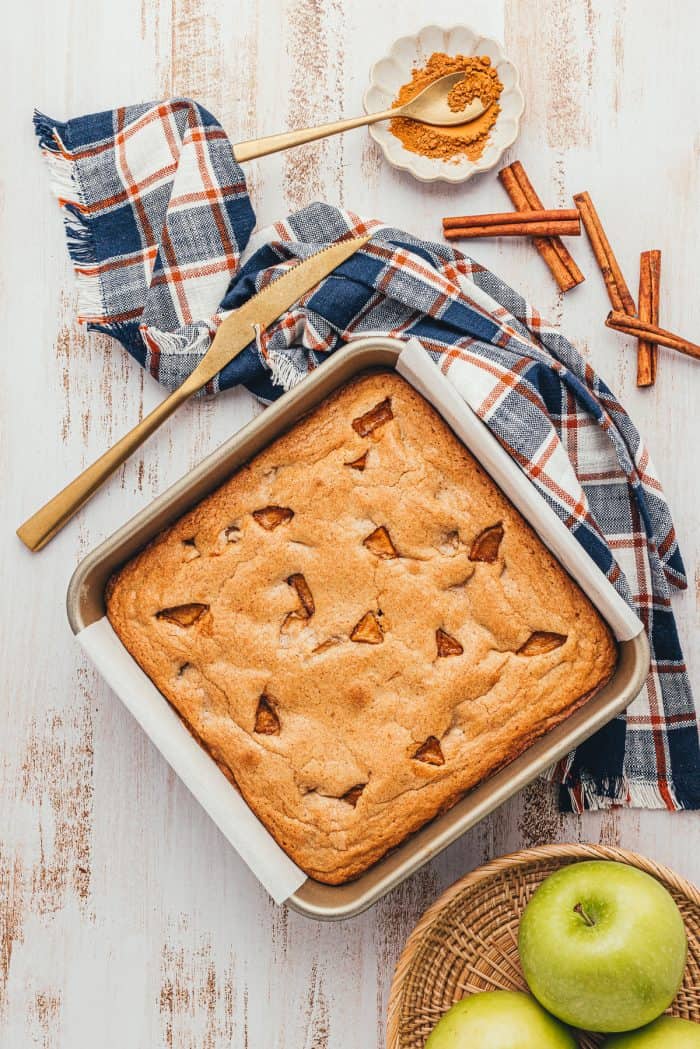 A square baking pan with baked apple pie blondies and a bowl of green apples.