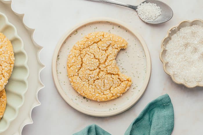 A white plate with a brown butter cookie with a bite taken out of it.