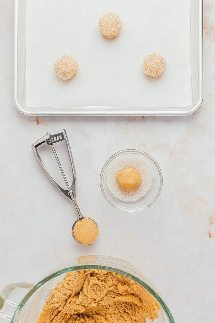 A small glass bowl with sanding sugar and a cookie sheet with balls of cookie dough.