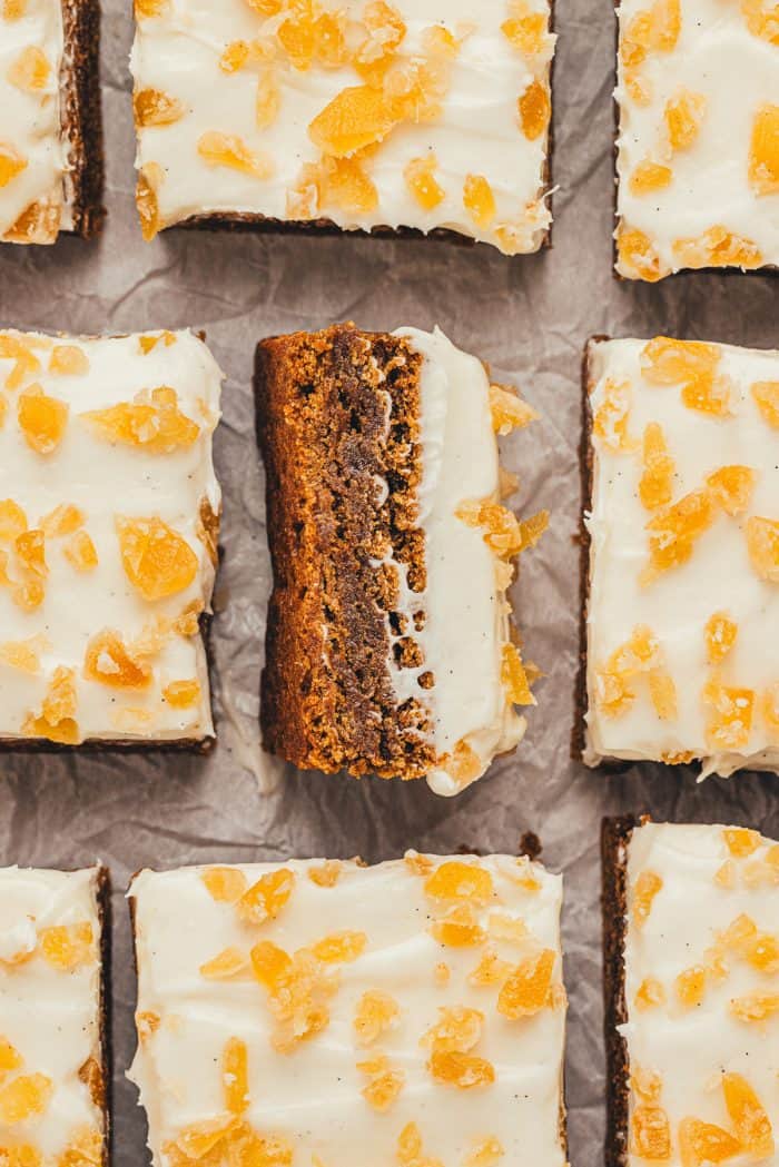 The gingerbread bars with frosting and candied ginger cut into squares and one square is turned over.