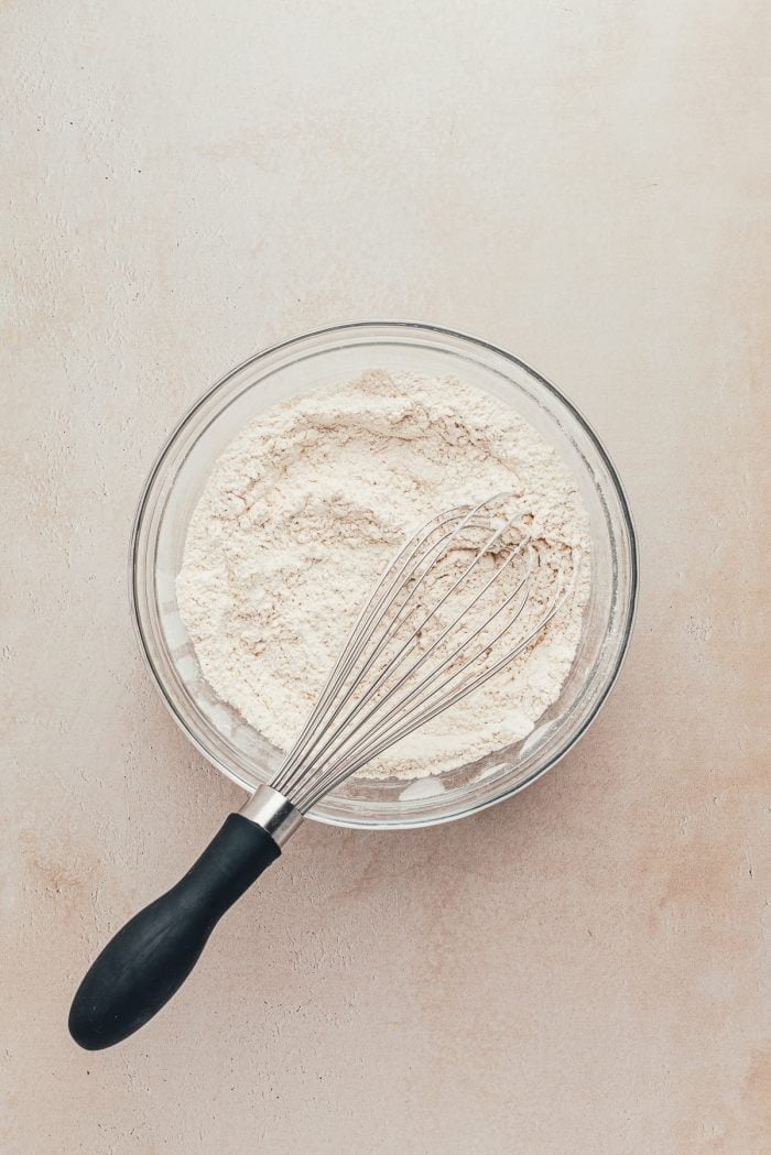 A glass bowl with a whisk and the dry ingredients for making gingerbread bars.