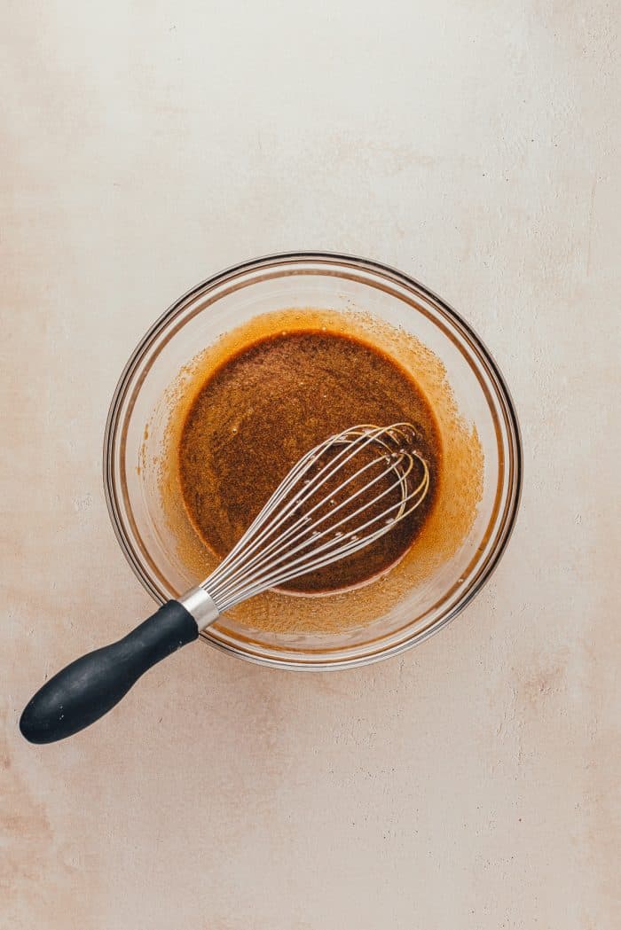 A glass bowl with a whisk and the dry ingredients mixed with melted butter, spices, and molasses. 