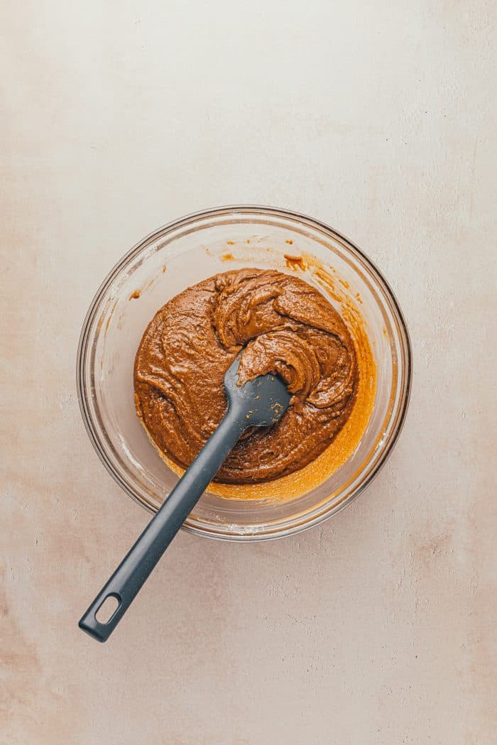 A glass bowl with the gingerbread batter in it with a spatula.