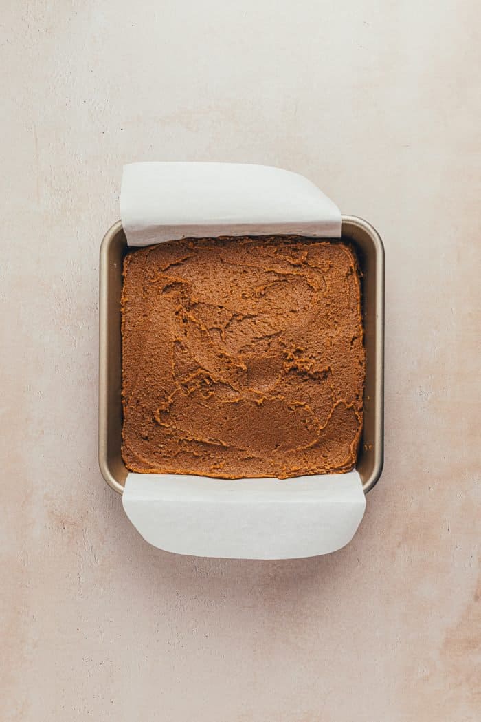 A baking tray with the raw gingerbread batter and parchment paper overhanging it.