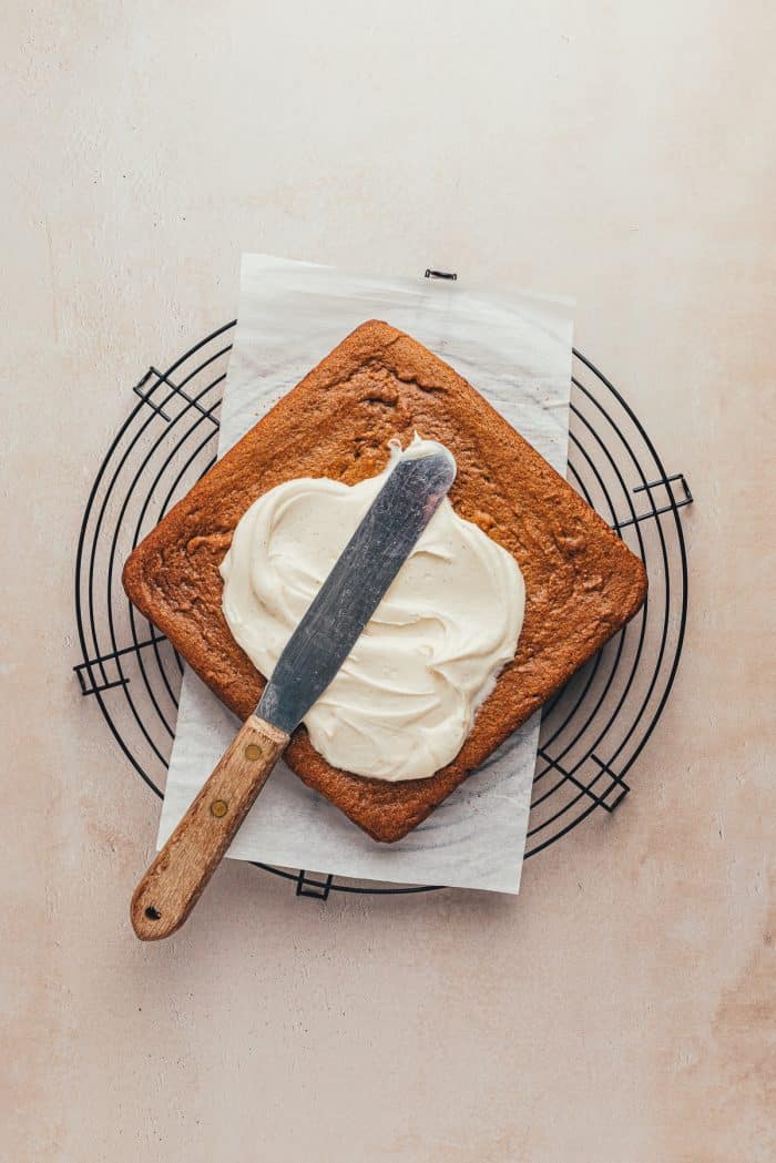 Baked gingerbread bars with frosting being frosted over them.