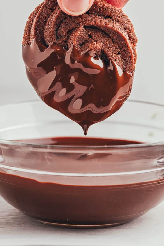 A chocolate orange butter cookie being dipped into melted chocolate.