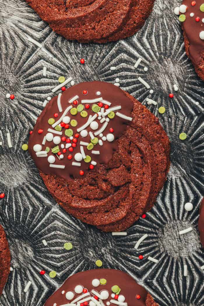 A chocolate dipped chocolate orange cookie with sprinkles on an old-fashioned cookie tray.