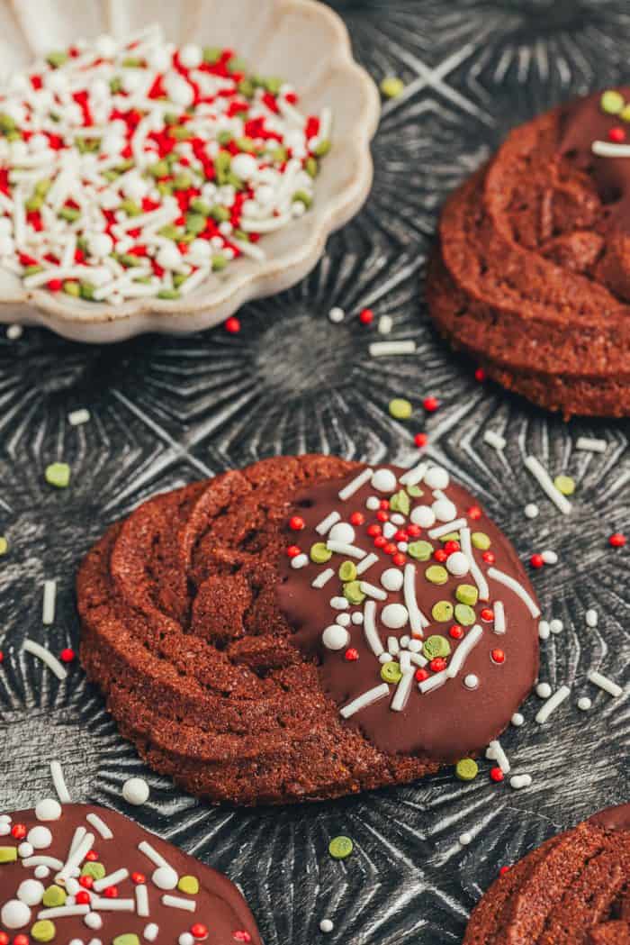 A chocolate dipped chocolate orange cookie with sprinkles on an old-fashioned cookie tray.