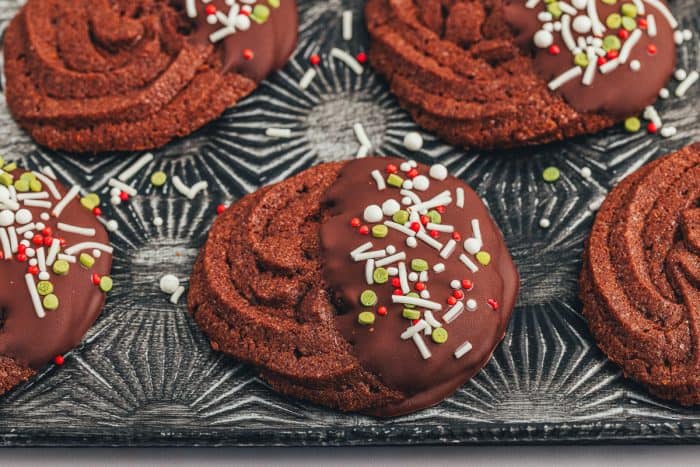 A chocolate dipped chocolate orange cookie with sprinkles on an old-fashioned cookie tray.