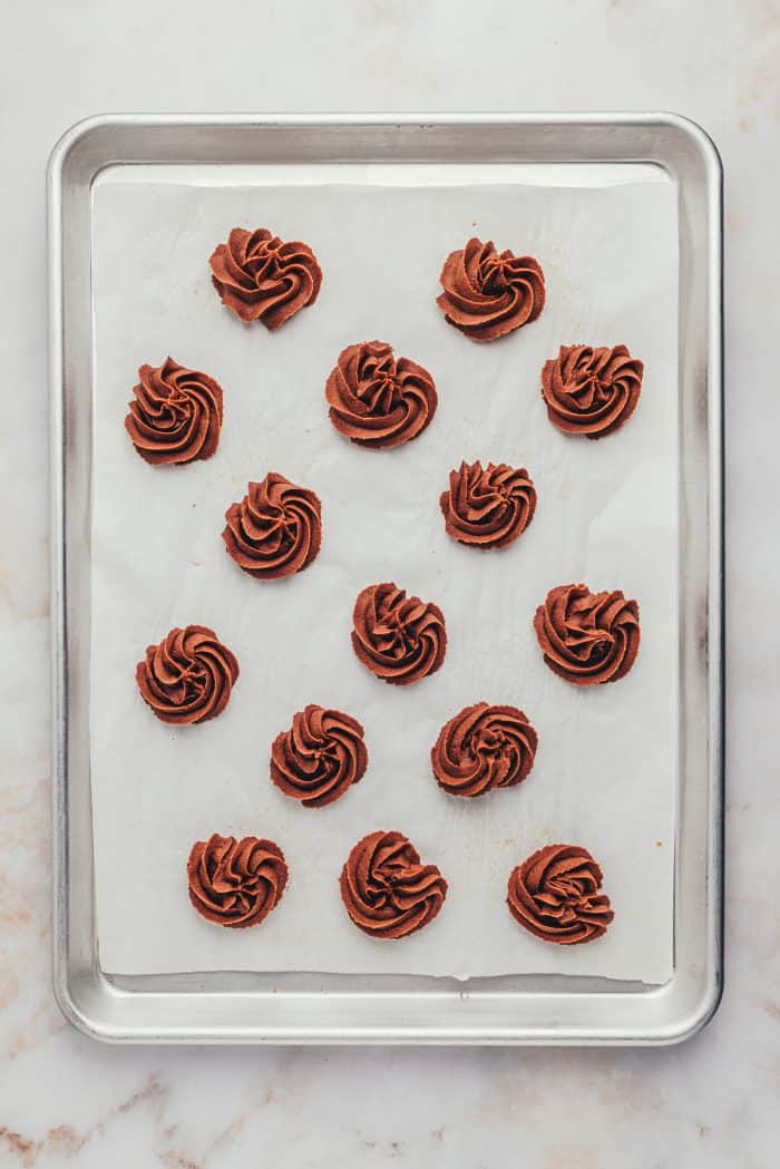 The cookies piped onto a parchment-lined baking tray.