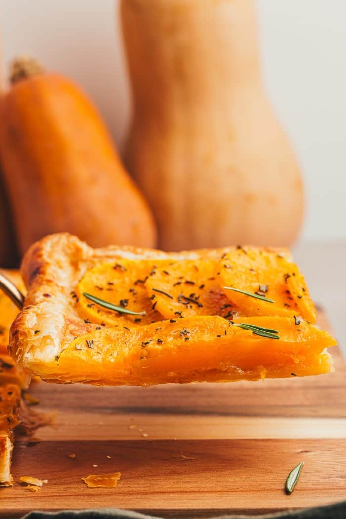 A slice of butternut tart with two butternut squashes in the background.