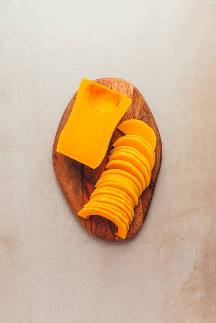 The butternut squash is peeled and sliced on a wooden tray.