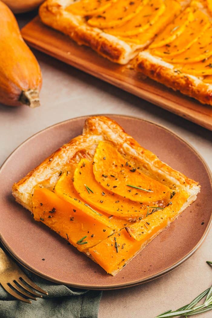 An image of a slice of butternut squash on a brown plate with a gold fork.