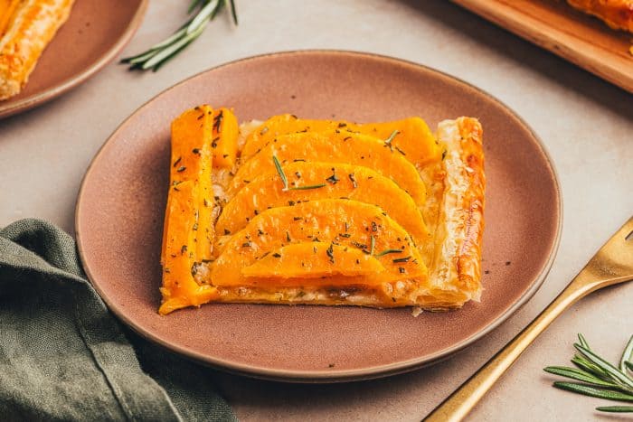 An image of a slice of butternut squash on a brown plate with a gold fork.