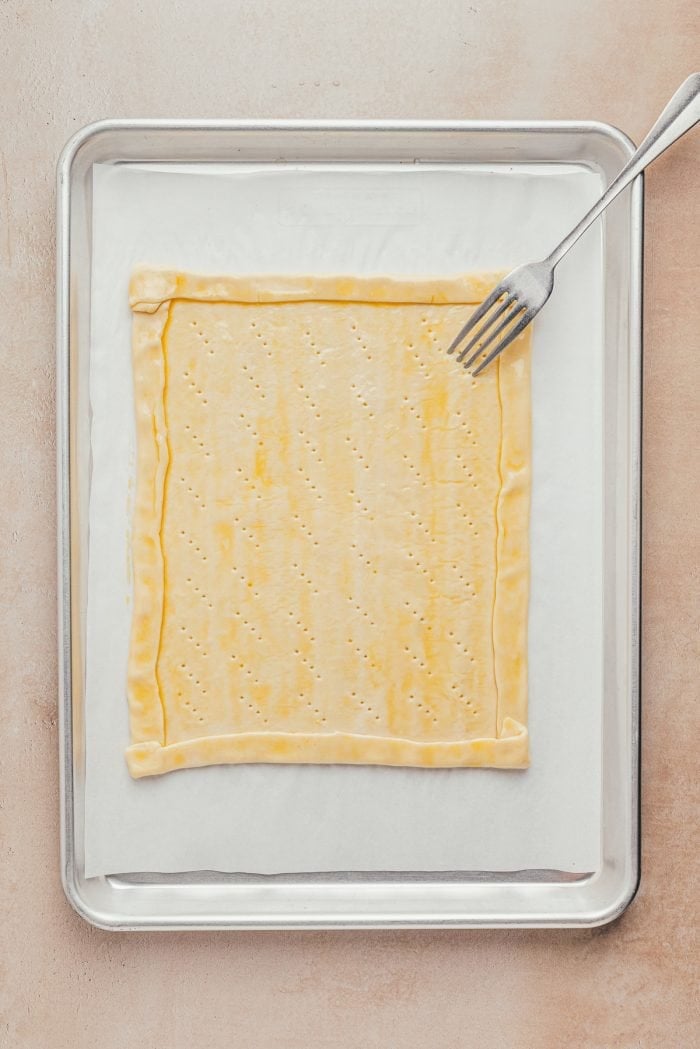 Puff pastry rolled out on a baking sheet with the edges turned in to make a crust and a fork.